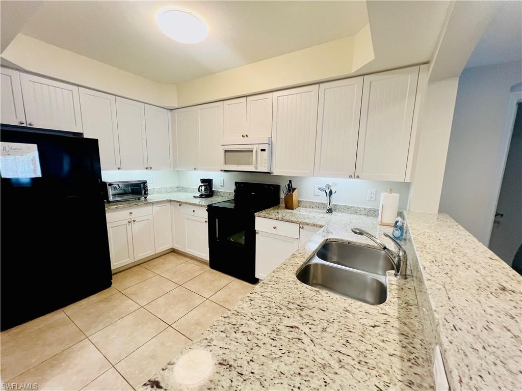 Kitchen featuring a toaster, white cabinetry, light tile patterned flooring, black appliances, and a sink
