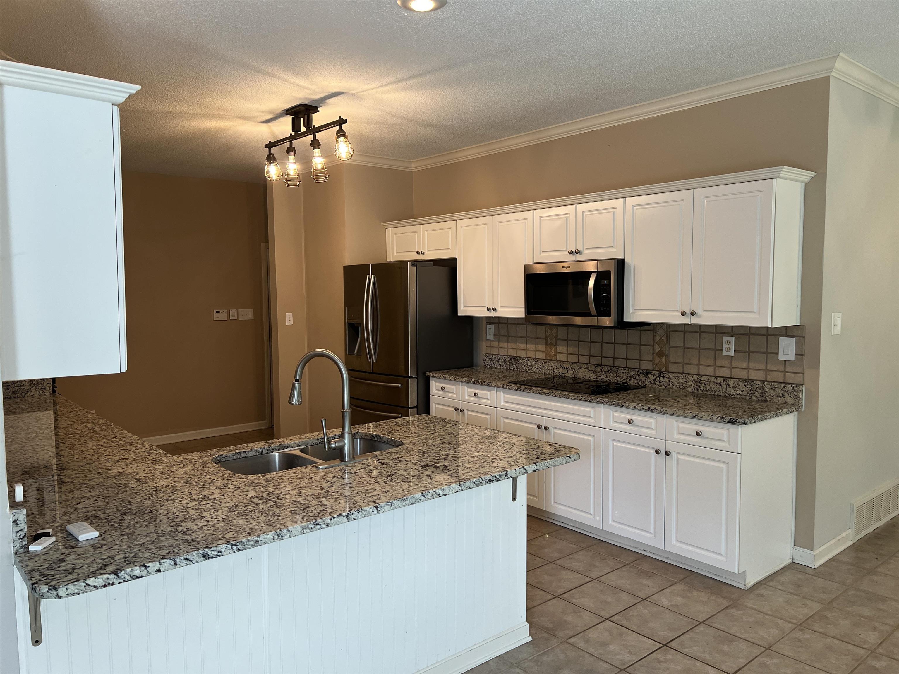 455 Hunters Mill Cove Collierville, TN 38017 - Photo 3 of 10 Kitchen featuring a peninsula, light stone counters, a textured ceiling, white cabinetry, and crown molding