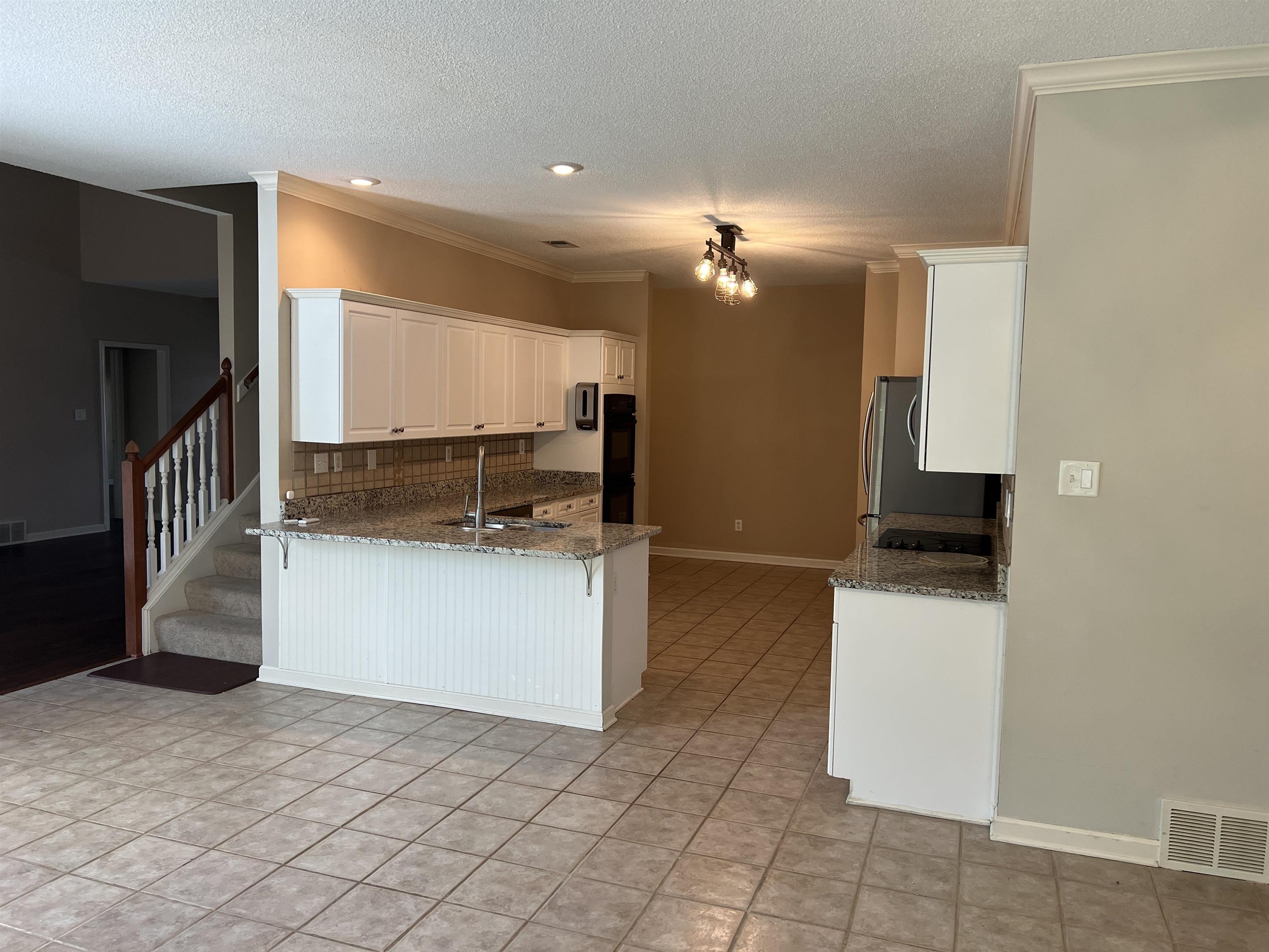 455 Hunters Mill Cove Collierville, TN 38017 - Photo 4 of 10 Kitchen with dark stone countertops, white cabinetry, a textured ceiling, a peninsula, and ornamental molding