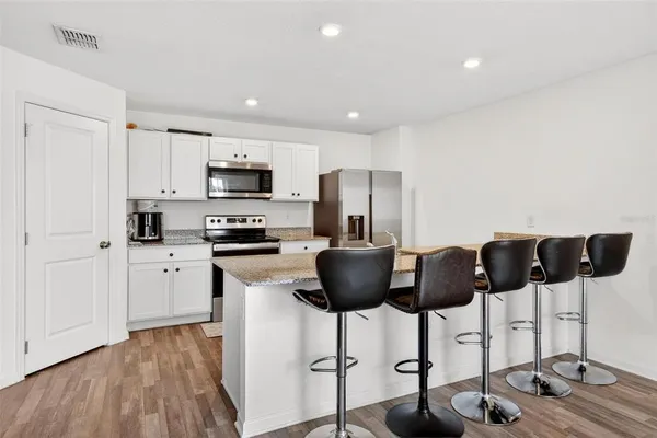 a kitchen with stainless steel appliances granite countertop a refrigerator a stove a microwave a dining table and chairs with wooden floor