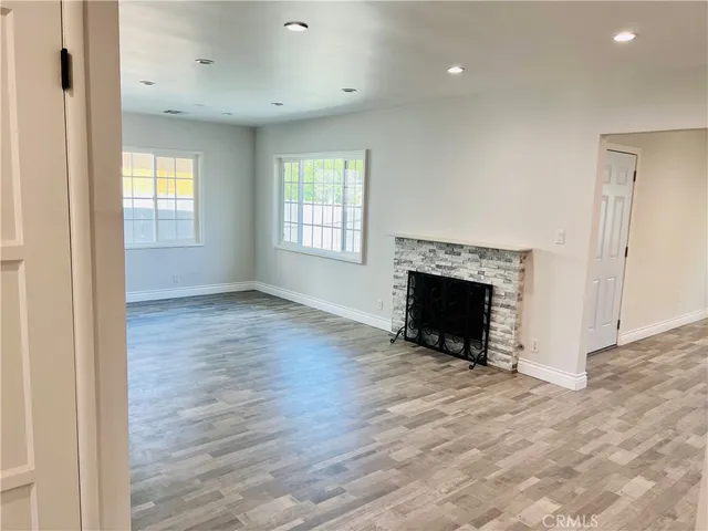 an empty room with wooden floor fireplace and windows