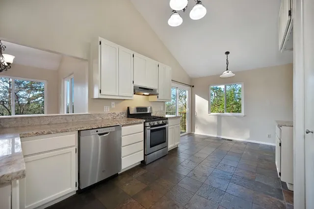 a kitchen with kitchen island granite countertop a stove a sink and a dishwasher with white cabinets