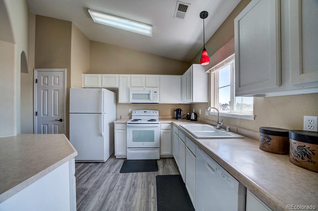 3875 Strawberry Field Grove Colorado Springs, CO 80906 - Photo 30 of 50 a kitchen with a sink dishwasher a refrigerator a stove and white cabinets with wooden floor
