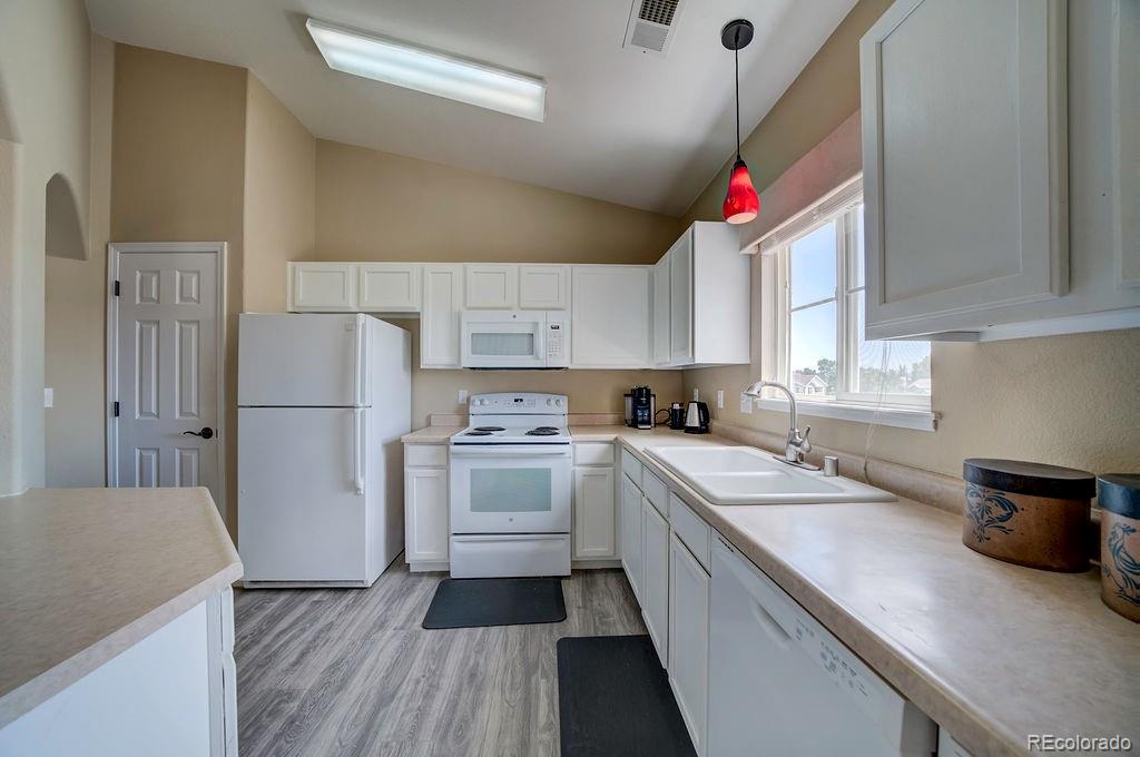 3875 Strawberry Field Grove Colorado Springs, CO 80906 - Photo 31 of 50 a kitchen with a sink dishwasher a refrigerator a stove and white cabinets with wooden floor