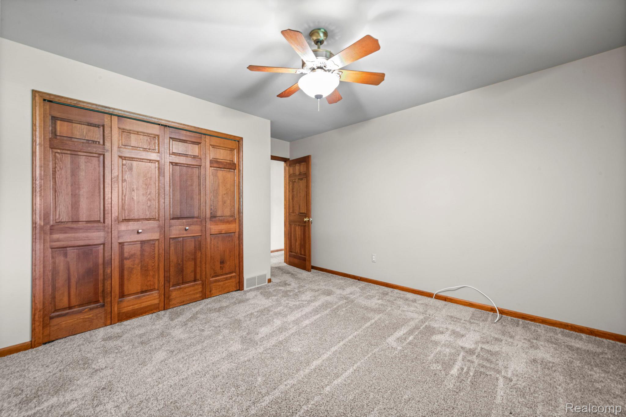 21580 Georgetown Road Trenton, MI 48183 - Photo 17 of 36 Room featuring light-colored walls, wood-finish bi-fold closet doors, a wood-finish interior door, light gray patterned carpet, and a ceiling fan with integrated lighting