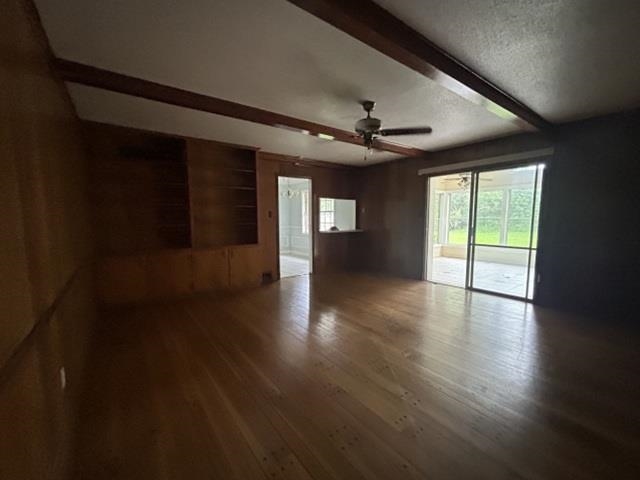 Spacious room featuring wood-finish flooring, wood paneling, and an exposed beam ceiling