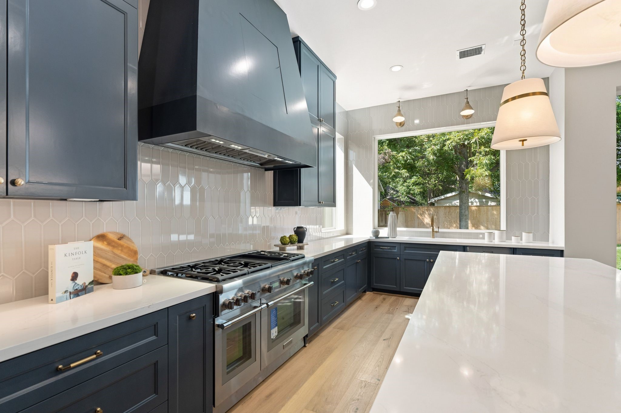 711 East 12th Street Houston, TX 77008 - Photo 21 of 47 Custom cabinetry in Sherwin-Williams Outerspace contrasts beautifully with Silestone Ethereal Glow quartz counters and a ceiling-height picket tile backsplash. Brass pendants add warmth, while a 48-inch Thermador range brings serious cooking capability.
