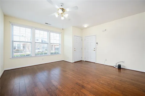 an empty room with wooden floor chandelier fan and windows
