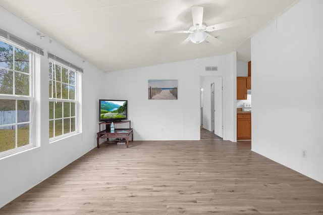 wooden floor in an empty room with a window and a kitchen