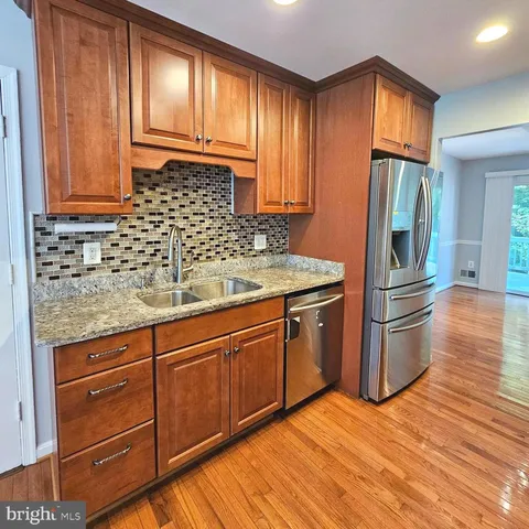 a kitchen with stainless steel appliances granite countertop a refrigerator a stove a sink and dishwasher with wooden cabinets
