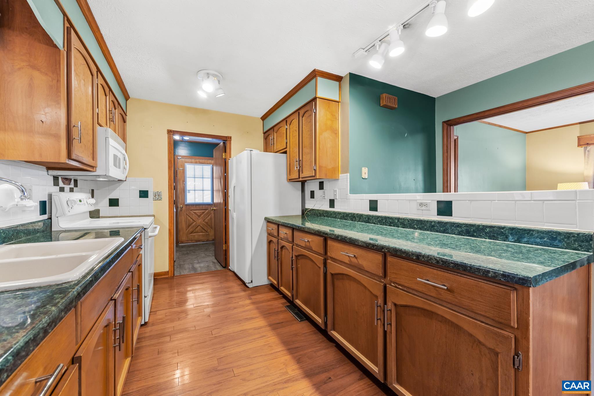 987 Matthew Mill Road Ruckersville, VA 22968 - Photo 12 of 63 Enjoy this spacious galley kitchen with warm wood cabinets, marble green counters, and durable wood floors. A convenient back door provides easy access, and the open counter connects to the living room.