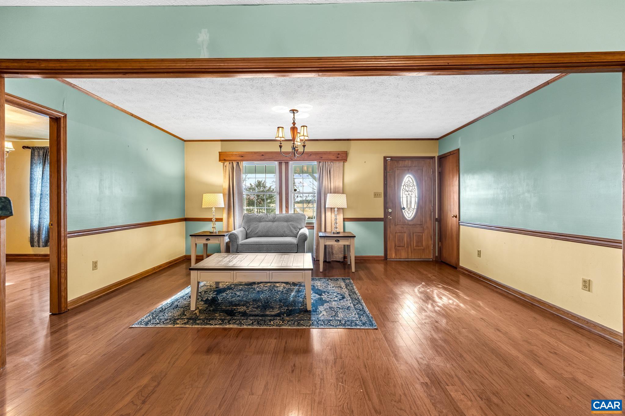 987 Matthew Mill Road Ruckersville, VA 22968 - Photo 15 of 63 Step into a bright, welcoming living space featuring gleaming wood floors, charming two-tone walls, and a classic wood trim. The glass-panel front door and stylish chandelier create a warm, inviting atmosphere.