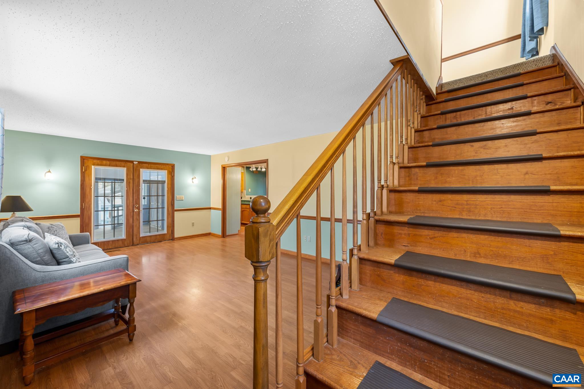 987 Matthew Mill Road Ruckersville, VA 22968 - Photo 31 of 63 Step inside to a bright, open family room space featuring rich wood floors and a classic staircase. French doors lead to an outdoor retreat, while an open doorway connects to the kitchen/dining area. Enjoy the charming two-tone walls.