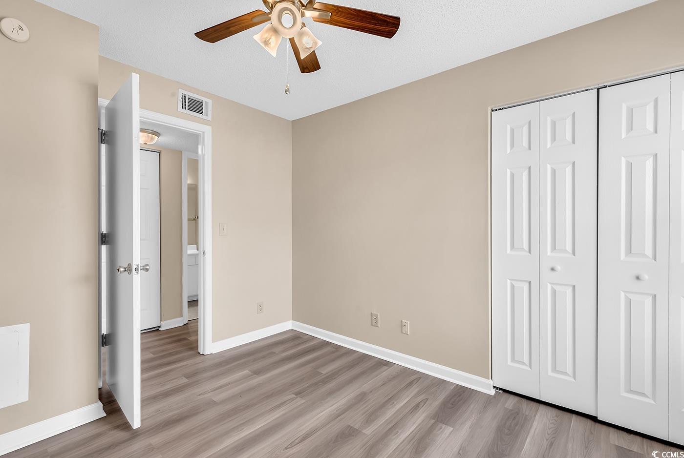 8796 Chandler Drive, Unit F Surfside Beach, SC 29575 - Photo 12 of 21 Unfurnished bedroom with light wood-style floors, ceiling fan, a closet, and a textured ceiling