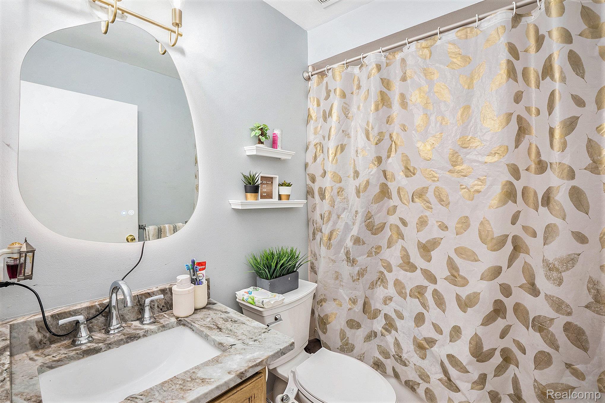 5477 Victory Circle Sterling Heights, MI 48310 - Photo 17 of 32 Bathroom featuring a vanity with a stone-finish countertop and undermount sink, illuminated mirror, and a full bathtub with a shower curtain rod