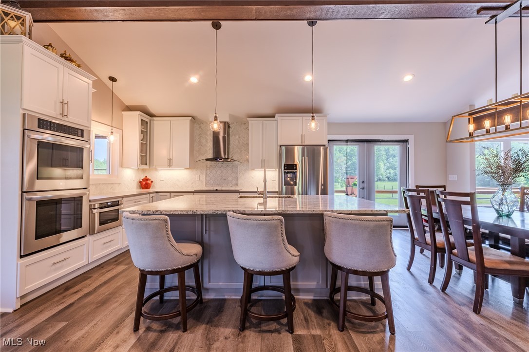 6268 Summers Road Windsor, OH 44099 - Photo 17 of 49 Kitchen with appliances with stainless steel finishes, wall chimney range hood, a kitchen island with sink, tasteful backsplash, and white cabinets