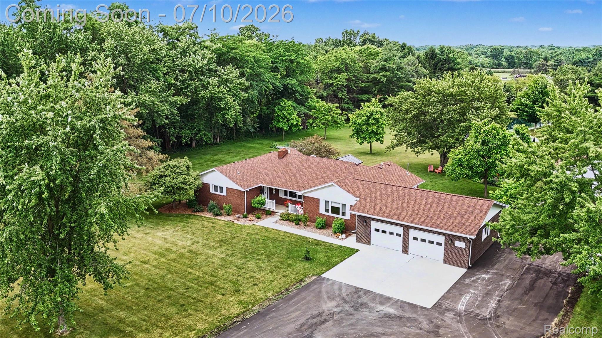 2180 Hurst Road St. Clair, MI 48079 - Photo 36 of 39 Red brick ranch home with a brown shingle roof, featuring a two-car attached garage with white doors, an asphalt driveway, and expansive green lawns surrounded by mature trees