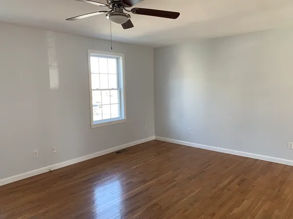 an empty room with wooden floor chandelier fan and windows