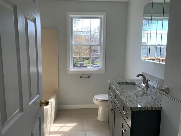 a bathroom with a granite countertop sink a toilet and a window