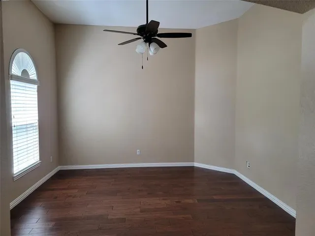 an empty room with wooden floor fan and windows