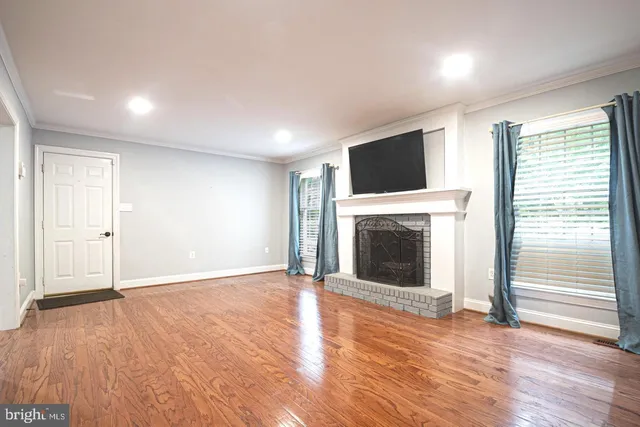 an empty room with wooden floor fireplace and windows