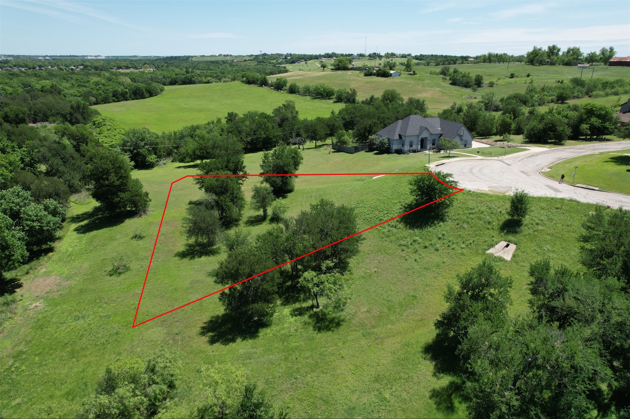 1700 Tanner Loop Taylor, TX 76574 - Photo 4 of 32 Expansive land parcel featuring a verdant, undulating landscape with scattered mature trees and a partial border defined by red lines