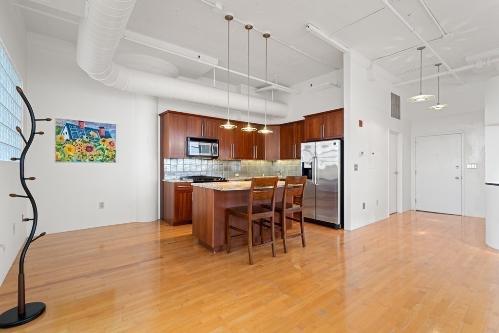 437 D Street, Unit 6A Boston, MA 02210 - Photo 10 of 26 a kitchen with stainless steel appliances kitchen island granite countertop a refrigerator a stove a sink a dining table and chairs with wooden floor
