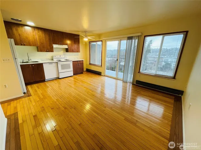 a view of a kitchen with kitchen island wooden floors stainless steel appliances a sink and a large window
