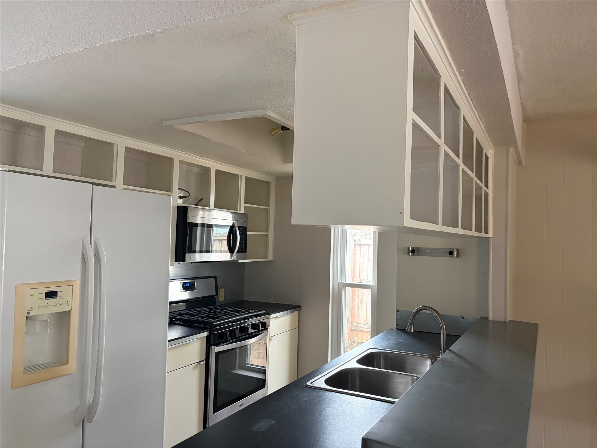 7404 Bethune Avenue, Unit B Austin, TX 78752 - Photo 6 of 13 Kitchen featuring dark countertops, stainless steel appliances, open shelves, glass insert cabinets, and a textured ceiling