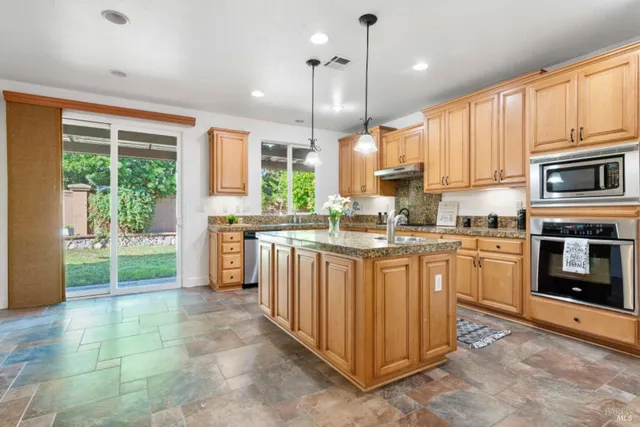 a kitchen with stainless steel appliances granite countertop a stove a sink a center island and a wooden floor
