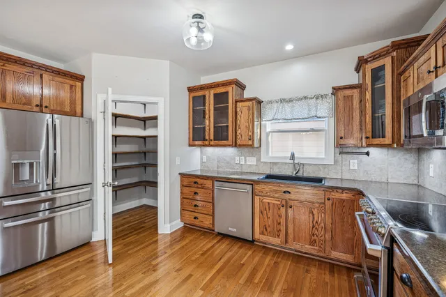 a kitchen with stainless steel appliances granite countertop a refrigerator a sink dishwasher a stove and white countertops with wooden floor