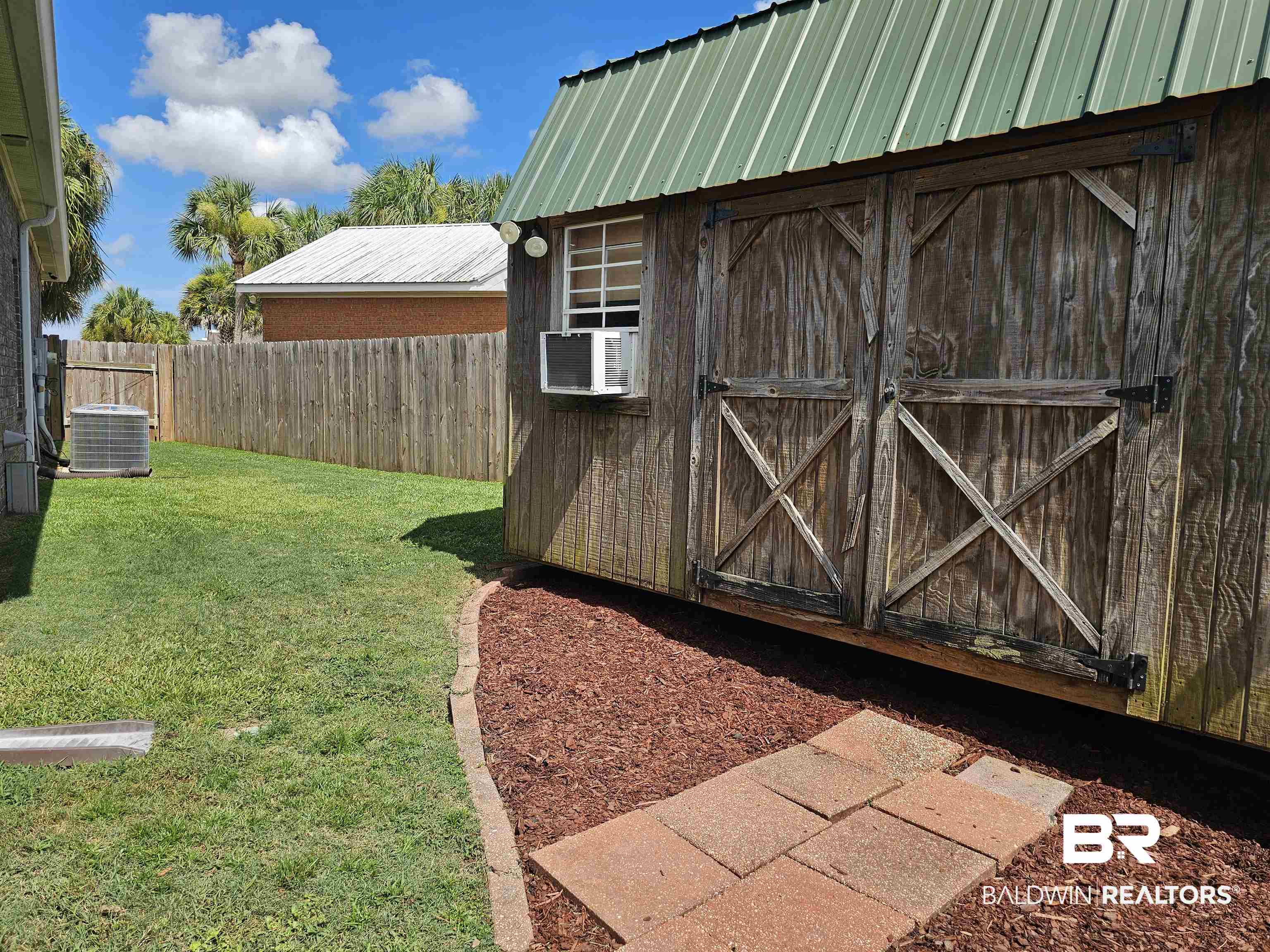1181 Sloane Cove Foley, AL 36535 - Photo 6 of 10 Wood-sided utility shed featuring a green metal roof, a window-mounted air conditioning unit, and double barn-style doors with X-bracing