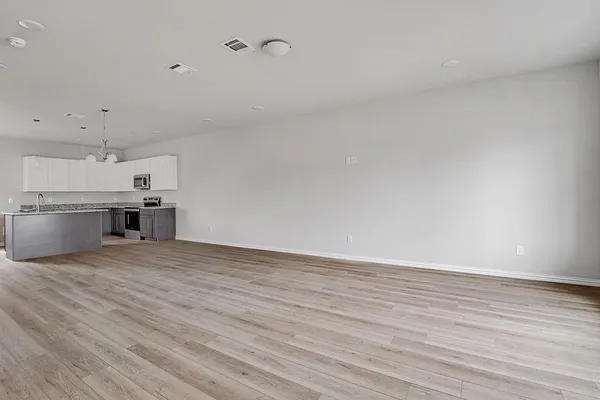 an empty room with wooden floor kitchen view and a window