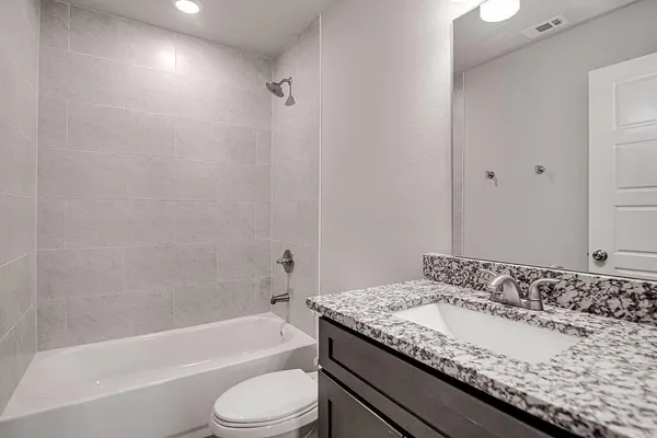 a bathroom with a granite countertop bathtub sink vanity mirror and toilet