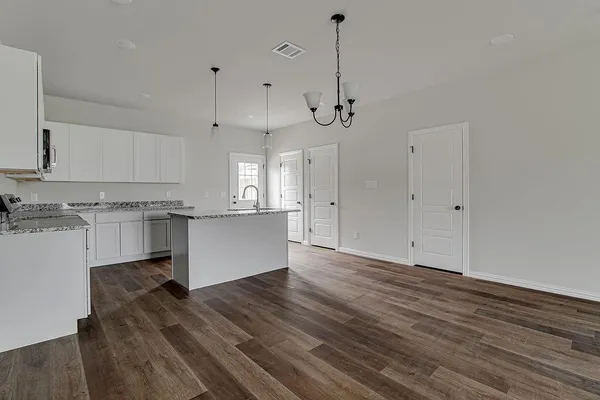 a view of an empty room with kitchen and window