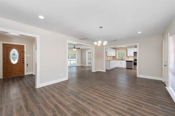 a view of an empty room and kitchen with wooden floor