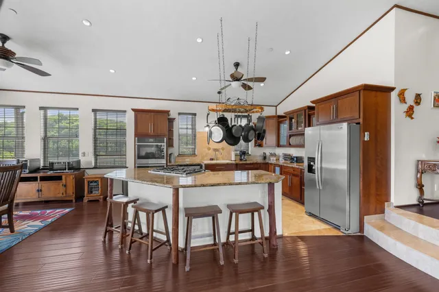 a kitchen with stainless steel appliances granite countertop a refrigerator a stove top oven a dining table and chairs with wooden floor