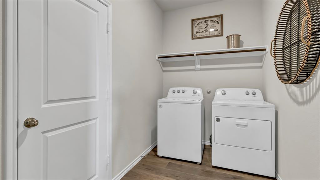 124 Pheasant Run Road Terrell, TX 75160 - Photo 31 of 35 Dedicated laundry area featuring a white door with brass hardware, wood-finish flooring, and a wall-mounted shelf above the appliances