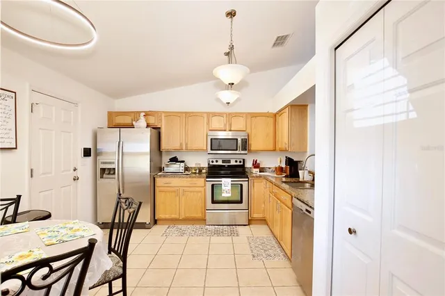 a kitchen with stainless steel appliances granite countertop a stove a refrigerator a sink dishwasher a dining table and chairs with wooden floor