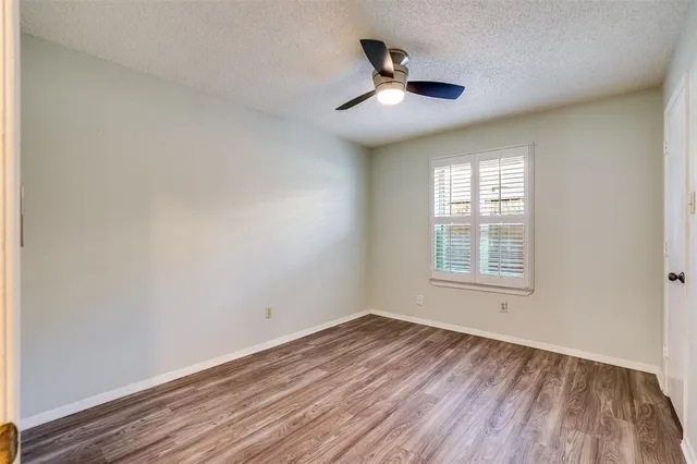 an empty room with wooden floor ceiling fan and windows