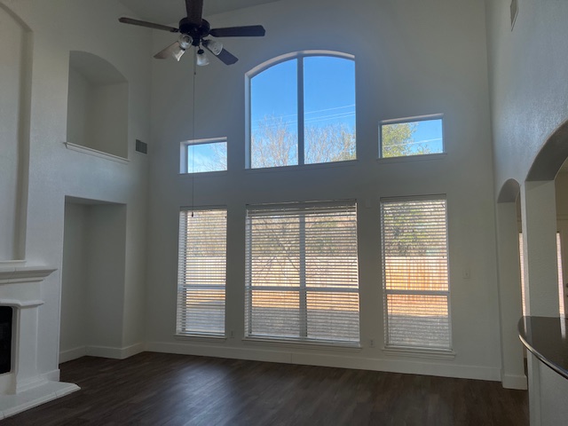1374 Red Stag Place Round Rock, TX 78665 - Photo 12 of 34 Unfurnished living room with arched walkways, dark wood-style flooring, ceiling fan, a fireplace with raised hearth, and a high ceiling
