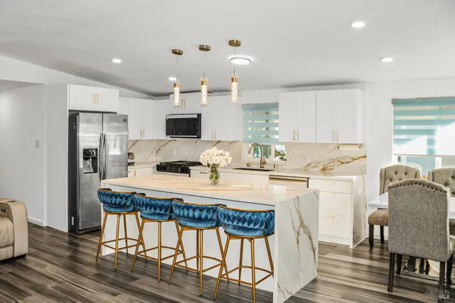 a kitchen with kitchen island granite countertop a dining table chairs refrigerator and microwave