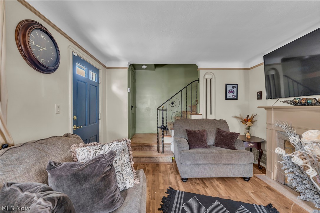 3962 Grosvenor Road South Euclid, OH 44118 - Photo 5 of 27 Living area featuring wood-finish flooring, a fireplace with a light-toned mantel, light beige wall paint with white trim, and a prominent dark blue entry door with transom window