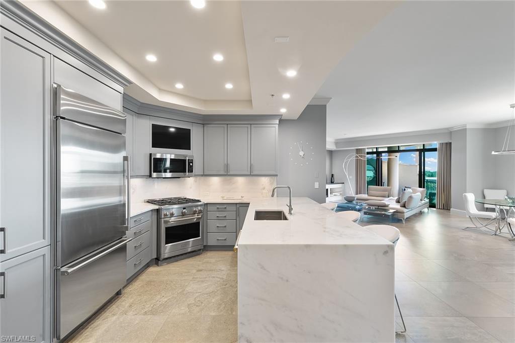 9123 Strada Place, Unit 7510 Naples, FL 34108 - Photo 11 of 38 Kitchen with gray cabinets, light stone countertops, a peninsula, a breakfast bar area, and premium appliances