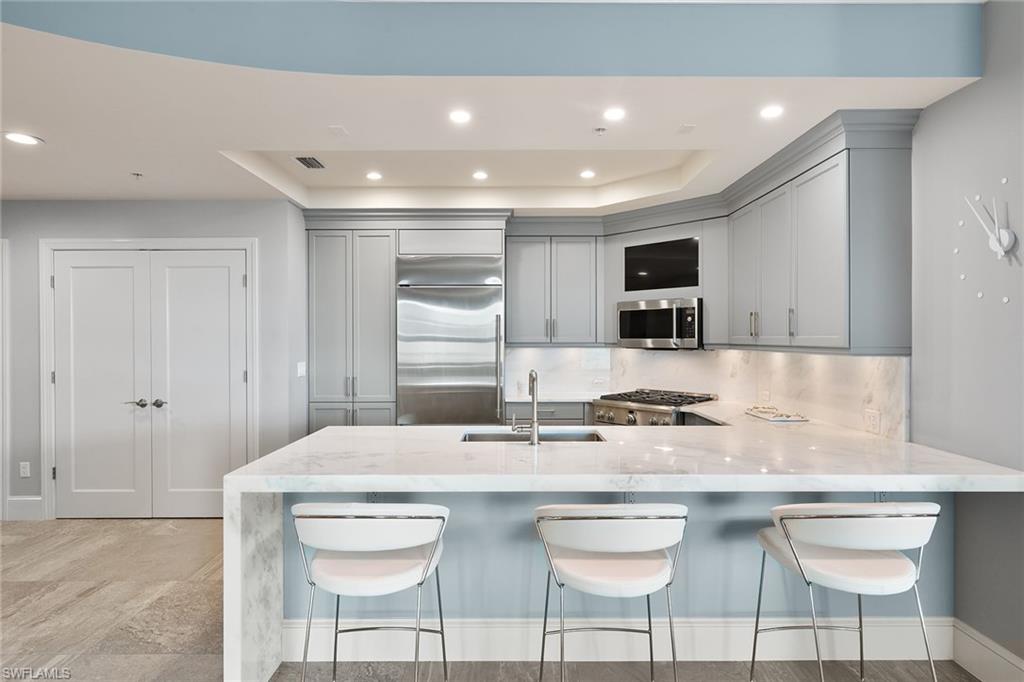 9123 Strada Place, Unit 7510 Naples, FL 34108 - Photo 7 of 38 Kitchen with light stone countertops, a breakfast bar area, a peninsula, recessed lighting, and a raised ceiling