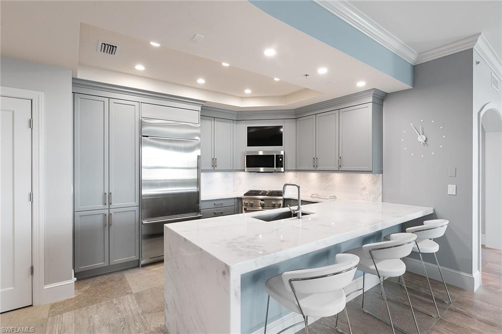 9123 Strada Place, Unit 7510 Naples, FL 34108 - Photo 9 of 38 Kitchen featuring gray cabinetry, a breakfast bar area, light stone countertops, a peninsula, and stainless steel appliances