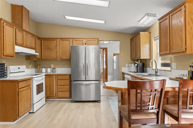 a kitchen with granite countertop a refrigerator a stove a sink dishwasher and white cabinets with wooden floor