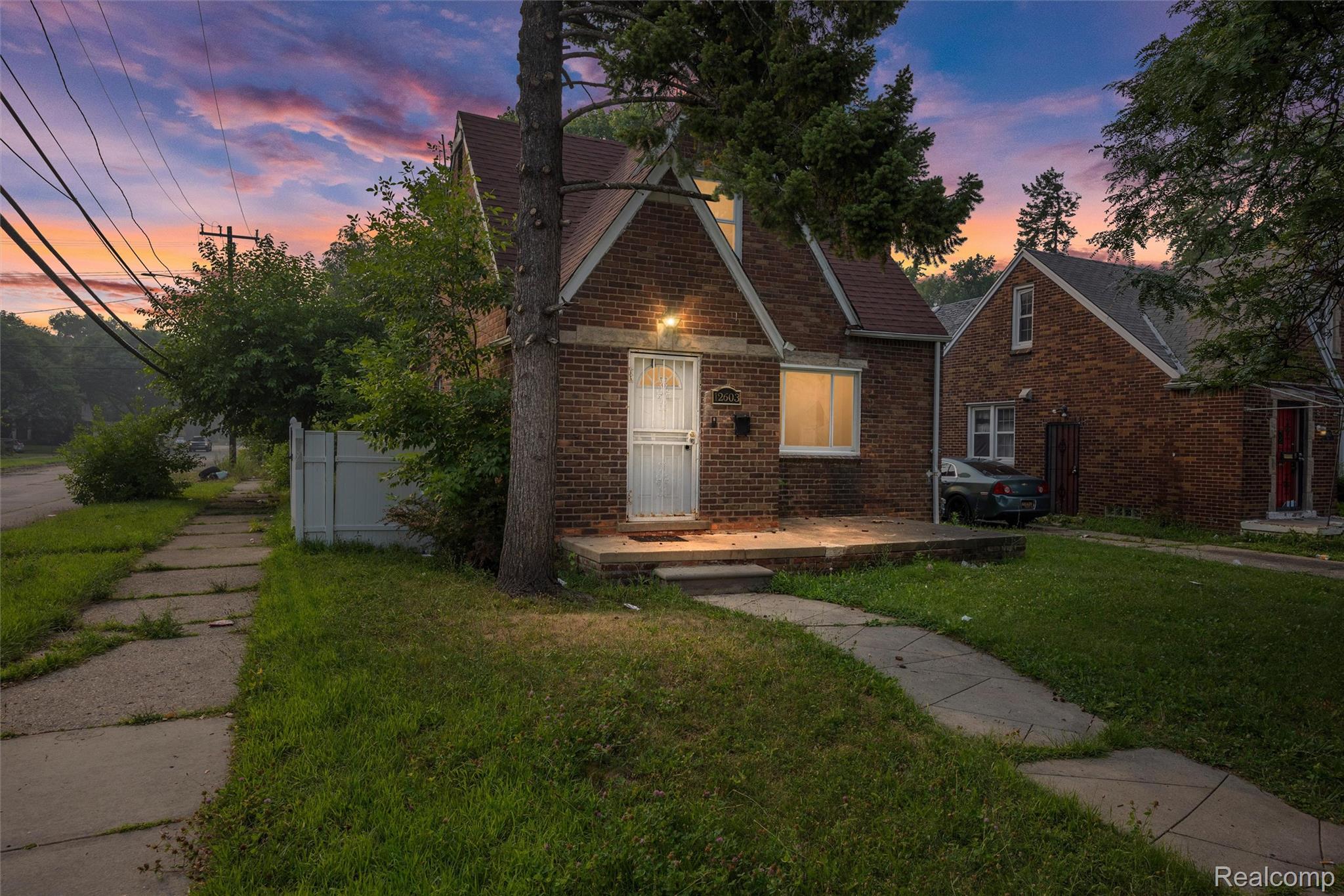 12603 Riad Street Detroit, MI 48224 - Photo 1 of 16 Brick exterior home featuring a gabled roofline, front porch, mature trees, and concrete walkways