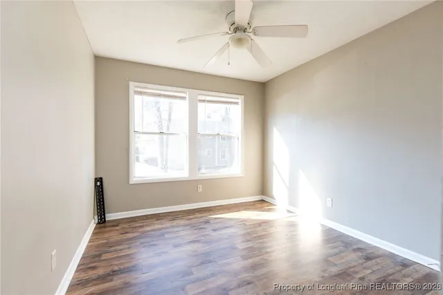 an empty room with wooden floor chandelier fan and windows