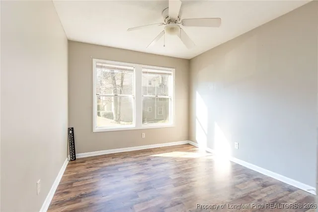 an empty room with wooden floor chandelier fan and windows